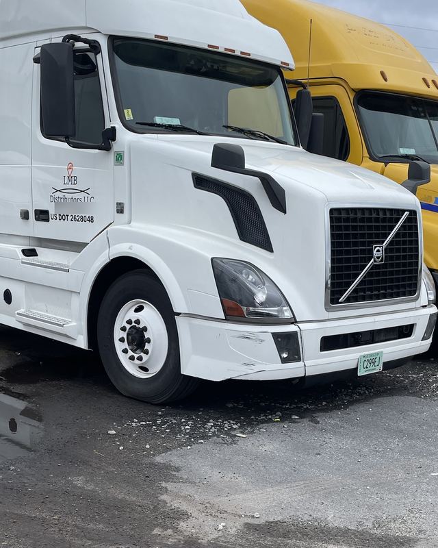White LMB Distributors Volvo sleeper parked beside a yellow Cascadia